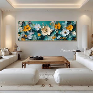 May include: Abstract painting of yellow and white flowers on a teal background. The painting is framed and hanging on a wall in a living room setting.