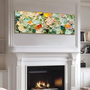 May include: Abstract painting with a textured, impasto style. The painting features a mix of green, yellow, orange, and pink colors. The painting is displayed above a fireplace in a white room.