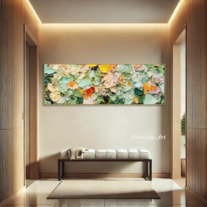 May include: Abstract painting with a textured, impasto style. The painting features a mix of green, yellow, pink, and orange colors. The painting is framed in a gold frame and is hanging on a white wall.