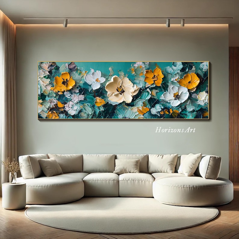 May include: Abstract painting featuring a vibrant floral design with yellow and white flowers on a teal background. The painting is framed and hanging on a wall above a white couch.
