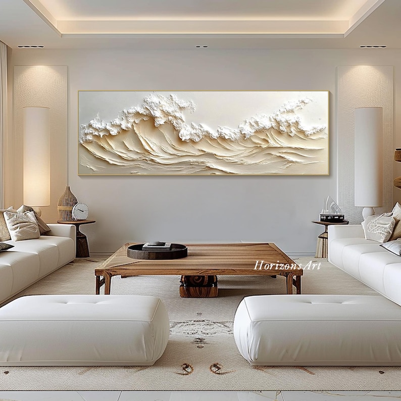 May include: A large, abstract painting of white waves on a cream background. The waves are textured and appear to be three-dimensional. The painting is framed in a thin, gold frame. The painting is hanging on a white wall in a living room setting.