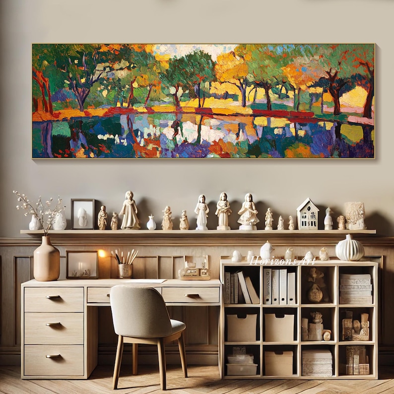 May include: A colorful abstract painting of a forest scene with trees reflected in a still body of water. The painting is framed in a gold frame and hangs on a wall above a desk and bookshelf.