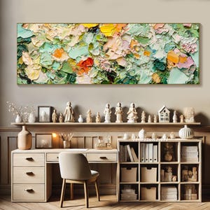 May include: A colorful abstract painting with a textured, impasto style. The painting features shades of green, yellow, orange, and pink. It is displayed on a wall above a wooden desk with a chair and shelves.