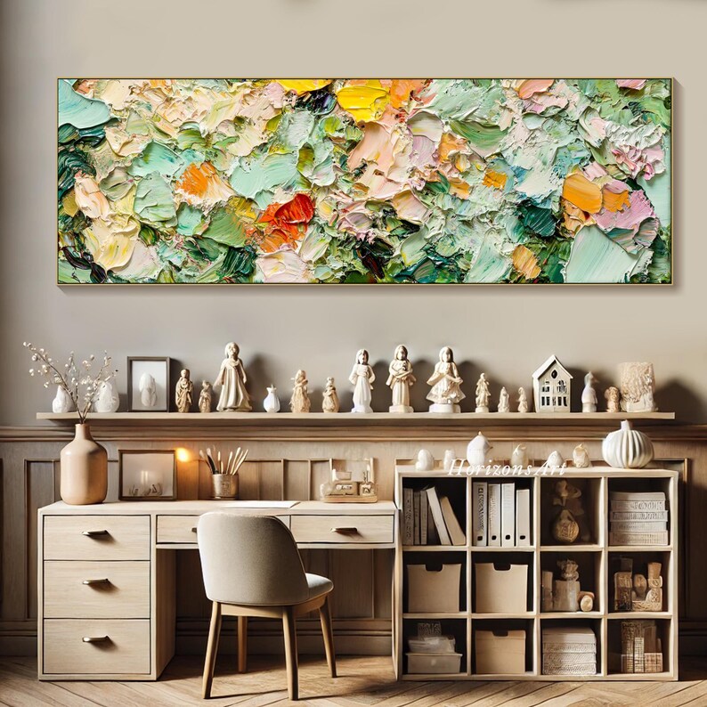 May include: A colorful abstract painting with a textured, impasto style. The painting features shades of green, yellow, orange, and pink. It is displayed on a wall above a wooden desk with a chair and shelves.