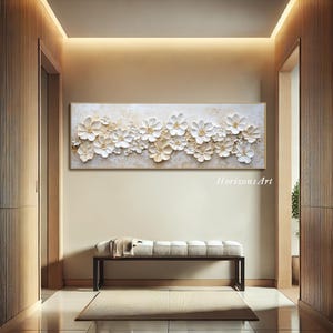 K&ouml;nnte beinhalten: Ein wei&szlig;es und goldenes 3D-Wandbild mit Blumen in einem strukturierten, erhabenen Design. Das Kunstwerk zeigt eine horizontale Anordnung von wei&szlig;en Blumen mit goldenen Akzenten auf einem cremefarbenen Hintergrund.