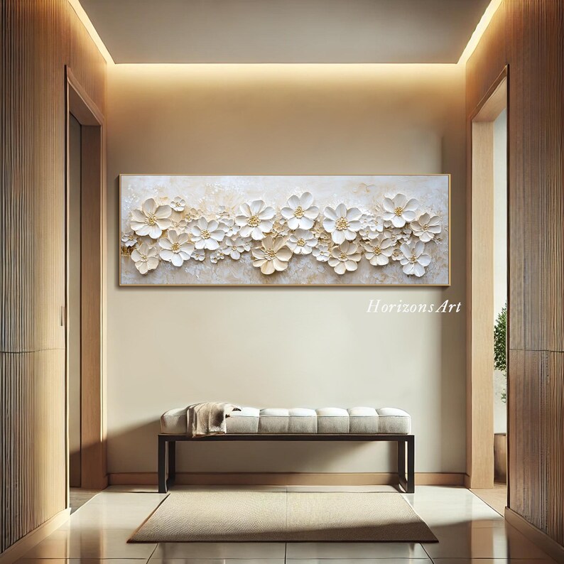K&ouml;nnte beinhalten: Ein wei&szlig;es und goldenes 3D-Wandbild mit Blumen in einem strukturierten, erhabenen Design. Das Kunstwerk zeigt eine horizontale Anordnung von wei&szlig;en Blumen mit goldenen Akzenten auf einem cremefarbenen Hintergrund.