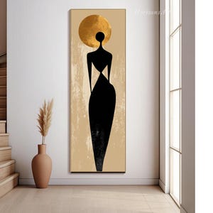 Puede incluir: Impresi&oacute;n art&iacute;stica abstracta que presenta una silueta negra de una figura con un halo dorado sobre un fondo beige. La figura lleva un vestido largo negro. La obra de arte est&aacute; enmarcada en un borde dorado y se exhibe en una habitaci&oacute;n bien iluminada.
