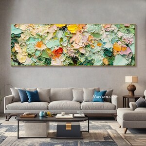 May include: Abstract painting with a textured, impasto style. The painting features a variety of colors, including green, yellow, pink, and orange. The painting is displayed on a wall above a gray sofa and a coffee table.