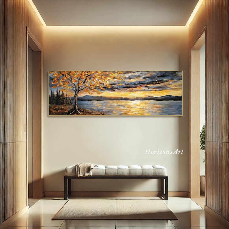 May include: A long, horizontal painting of a lake scene with a tree in the foreground. The tree has yellow and orange leaves. The lake is blue and reflects the sunset sky. The sky is a mix of blue, orange, and purple. The painting is framed in gold.