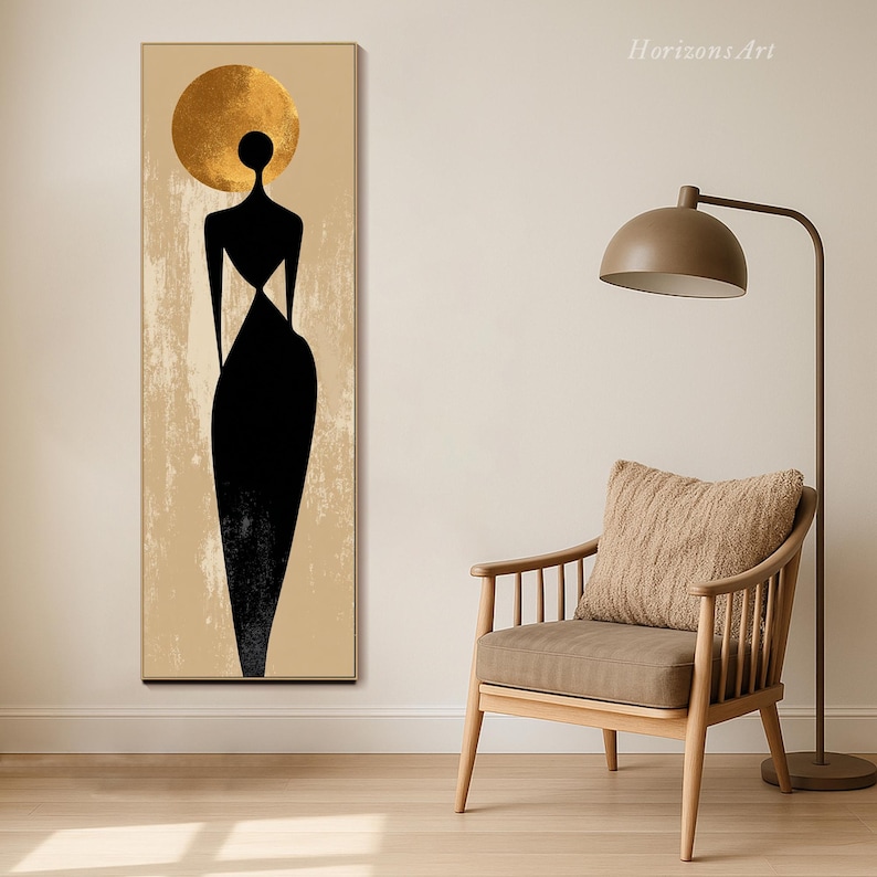 Puede incluir: Impresi&oacute;n art&iacute;stica abstracta que presenta una figura negra con un halo dorado sobre un fondo beige. La obra de arte es un rect&aacute;ngulo vertical, con el texto "Horizons Art" en la esquina superior derecha. La impresi&oacute;n se muestra cerca de una silla de madera y una l&aacute;mpara de pie.