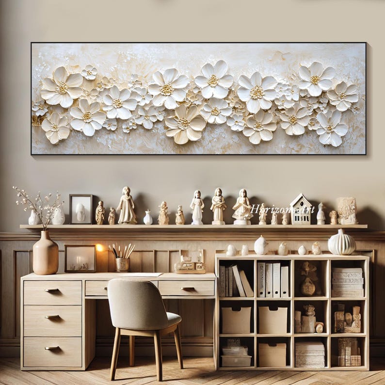 K&ouml;nnte beinhalten: Ein wei&szlig;er und goldener Wandkunstdruck mit floralem Motiv und einem 3D-Textileffekt. Der Druck zeigt eine horizontale Anordnung von stilisierten Blumen mit erhabenen Bl&uuml;tenbl&auml;ttern und einem dezenten goldenen Schimmer. Der Druck ist in einem schwarzen Rahmen gerahmt und wird an einer Wand &uuml;ber einem Schreibtisch mit einem B&uuml;cherregal und dekorativen Figuren ausgestellt.