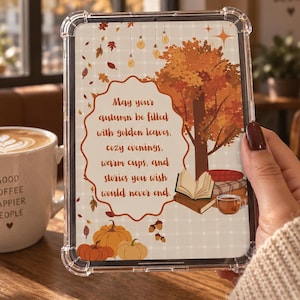 Könnte beinhalten: Eine transparente Tablet-Schutzhülle mit einem herbstlichen Motiv aus Baum, Kürbissen, einem offenen Buch und dem Text: May your autumn be filled with golden leaves, cozy evenings, warm cups, and stories you wish would never end.