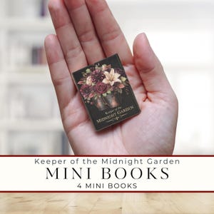 Könnte beinhalten: Ein Miniaturbuch mit schwarzem Einband, das ein Blumenarrangement aus dunkelroten, violetten und cremefarbenen Blüten in zwei Metalleimern zeigt. Der Text auf dem Einband lautet Keeper of the Midnight Garden in goldener Schrift. Klein und rechteckig.