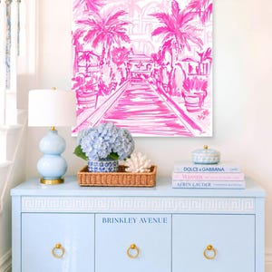 Hand-drawn pink coastal artwork depicting a Palm Beach–style walkway lined with palm trees, tropical foliage, and resort architecture; preppy, vibrant, tropical illustration with a summery coastal aesthetic