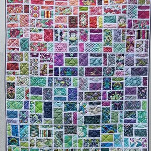 Könnte beinhalten: Eine Decke aus vielen verschiedenen Stoffquadraten, jedes mit einem einzigartigen Muster. Die Quadrate sind in einem Gittermuster angeordnet, und die Decke ist mit einem weißen Stoff eingefasst. Die Decke ist in verschiedenen Farben gehalten, darunter Rosa, Lila, Grün und Blau.