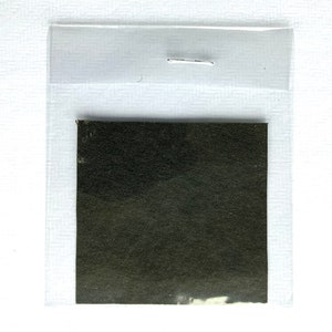 Può includere: Un piccolo campione di tessuto verde scuro all'interno di una custodia di plastica trasparente, fissato con una graffetta. Il tessuto ha un aspetto strutturato. Lo sfondo è bianco.