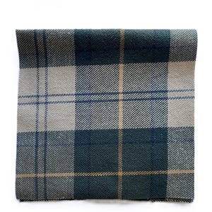 May include: Folded square of woven fabric with a plaid pattern. The design features a combination of dark teal, light gray, and tan lines. The fabric has a textured appearance, suggesting a wool or similar material.