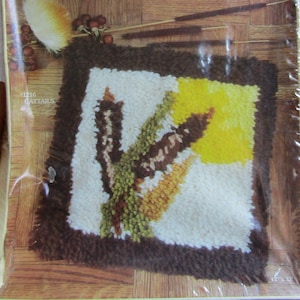 May include: Latch hook kit with a brown frame and a white, yellow, and green cattail design. The kit is labeled "#1216 Cattails" and "An ADCO Creation".