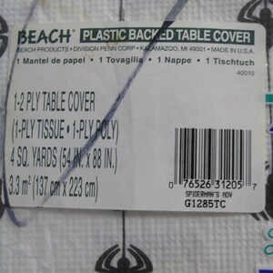 May include: White plastic-backed table cover with a spider web design. The label reads "BEACH PLASTIC BACKED TABLE COVER" and includes dimensions of 54 inches by 88 inches. The product is a 1-2 ply table cover.