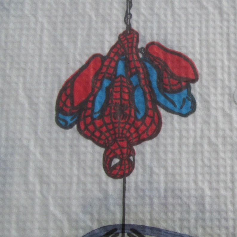 May include: A drawing of Spider-Man hanging upside down. The superhero is depicted in his classic red and blue suit with web detailing. The image is set against a textured white background.
