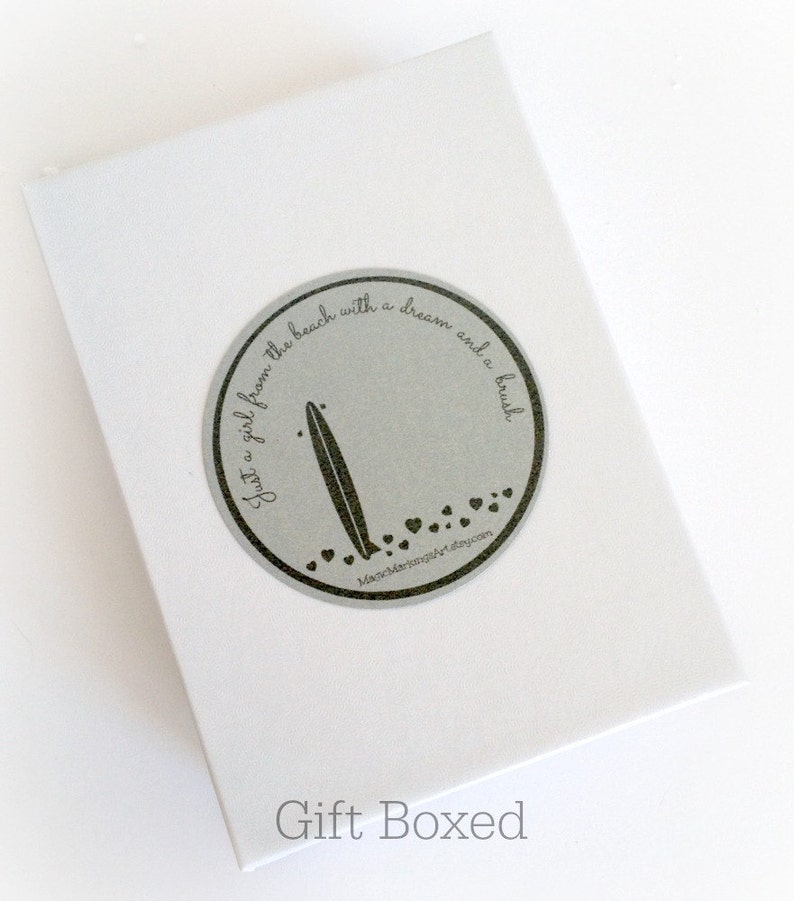 May include: A white gift box with a silver circle sticker that says "Just a girl from the beach with a dream and a brush" with a surfboard graphic and small hearts. The text "MancMarjungArt.etsy.com" is below the graphic. The box is labeled "Gift Boxed".