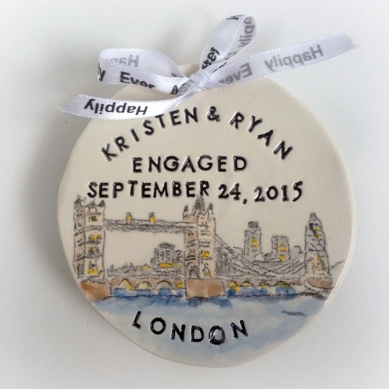 K&ouml;nnte beinhalten: Wei&szlig;er Keramik-Anh&auml;nger mit einer Schwarzwei&szlig;-Illustration der Tower Bridge in London. Der Anh&auml;nger ist mit dem Text "Kristen & Ryan Verlobt am 24. September 2015 London" verziert.