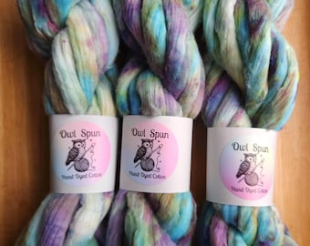 May include: Three skeins of hand-dyed cotton yarn featuring a variegated color palette of light blue, soft purple, and pale green. Each skein is secured with a white paper band displaying the text Owl Spun and Hand Dyed Cotton with an owl logo.
