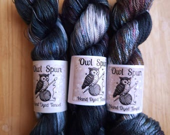 May include: Three skeins of hand-dyed Tencel yarn with a glossy finish. Each skein features a white paper label with the text Owl Spun and Hand Dyed Tencel, accompanied by a black and white illustration of an owl holding a knitting needle.