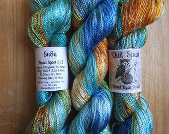 May include: Three skeins of hand-dyed Tencel sport weight yarn featuring a variegated color palette of bright blue, turquoise, and golden orange. Each skein has a paper label, with one reading SuSu Tencel Sport 3/2 and the other Owl Spun.