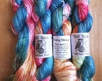 May include: Four skeins of Owl Spun hand-dyed Tencel sport yarn in a variegated colorway of bright blue, pink, orange, and yellow. The labels read Floating Hibiscus, Tencel Sport 3/2, 100g, 275 yards, and include care instructions.