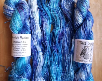 May include: Three skeins of hand-dyed Tencel sport yarn in shades of blue, purple, and white. The left label reads Moonlight Mystique Tencel Sport 3/2, 275 yards, 100g. The right label features an owl illustration and reads Owl Spun Hand Dyed Tencel.