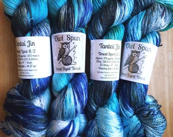 May include: Four skeins of hand-dyed Tencel yarn in shades of blue, teal, and black. Each skein features a white paper label with the brand name Owl Spun or Tantai Jin, an owl illustration, and printed product specifications including yardage.