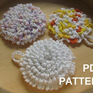 Può includere: Tre strofinacci all'uncinetto in una varietà di colori, tra cui bianco, giallo, arancione e rosa. Gli strofinacci sono disposti su una superficie di legno. Il testo "PDF PATTERN" è visibile nell'angolo in basso a destra dell'immagine.