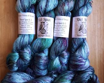 May include: Four skeins of hand-dyed Tencel yarn in shades of teal, blue, and purple. Each skein features a white paper label with an owl illustration and text including Dream Within A Dream, Owl Spun, Tencel Lace 8/2, and Tencel Sport 3/2.