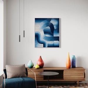 May include: A modern living room interior with a blue and white abstract painting hanging on the wall above a wooden console table. The console table has three vases on it, one red, one light blue, and one yellow. A blue armchair with a brown cushion sits in front of the console table. A black side table with a round top sits in front of the armchair.