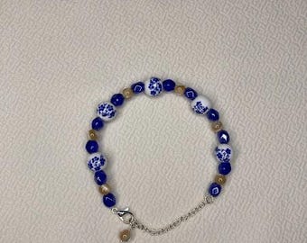 Pode incluir: Um bracelete de contas de porcelana azul e branco com um fecho de corrente de prata. As contas têm um padrão floral.