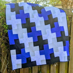 May include: A quilt with a geometric pattern of black, blue, and white plus signs. The quilt is made of fabric with a small white polka dot pattern.
