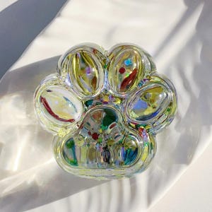 Puede incluir: Un plato de vidrio transparente con forma de huella de pata con purpurina arcoíris iridiscente en su interior. El plato tiene cinco secciones para guardar objetos pequeños.