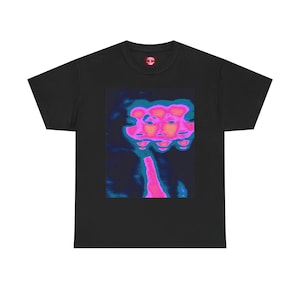May include: Black t-shirt featuring a vibrant, abstract graphic of multiple faces in shades of pink, blue, and teal. The design is centered on the shirt, with a small red logo on the upper back. The shirt is made of a soft, comfortable material.