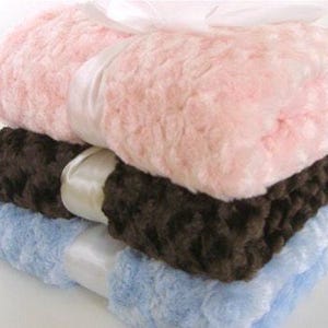 May include: Three plush blankets stacked on top of each other. The top blanket is pink, the middle blanket is brown, and the bottom blanket is light blue.