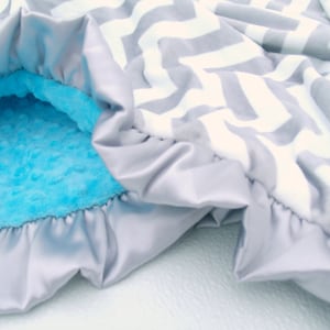 May include: A soft, gray and white chevron patterned baby blanket with a light blue minky lining. The blanket has a satin trim around the edges.