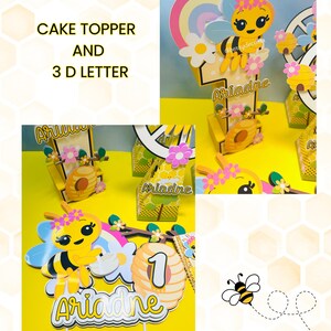 May include: A collection of bee-themed cake toppers and 3D letters. The toppers feature a yellow and black bee with a flower crown, a rainbow, and the name "Ariadne". The number "1" is also included. The background is yellow.