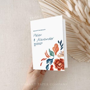 Może przedstawiać: Białe zaproszenie ślubne z niebieskimi i czerwonymi ilustracjami kwiatowymi. Tekst brzmi "Witamy na ślubie Helen & Alexander".