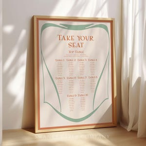Könnte beinhalten: Ein gerahmter Sitzplan mit dem Text "TAKE YOUR SEAT" in einer dekorativen Schriftart. Die Tabelle listet die Tische 1-10 auf, mit einem cremefarbenen Hintergrund, einem rostfarbenen Rand und türkisfarbenen Akzenten. Der Rahmen ist hellholzfarben.