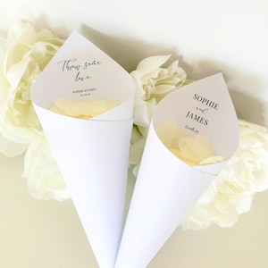 May include: Two white paper cones filled with white flower petals. The cones have text printed on them. The text on the left cone reads "Throw some love" and "Sophie & James 22.08.22". The text on the right cone reads "Sophie and James 22.08.22".