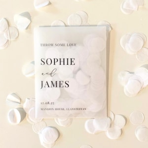 Op de afbeelding: Een transparant zakje gevuld met witte confetti, met de tekst "THROW SOME LOVE", de namen "SOPHIE and JAMES", de datum "12.08.25" en "MANSION HOUSE, LLANSTEFFAN" in zwart. Witte confetti is rondom het zakje verspreid.