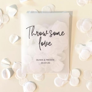 Op de afbeelding: Een doorschijnende envelop gevuld met witte confetti, met de tekst "Throw some love" in sierlijke letters. Onder de tekst staan de namen "OLIVIA & FREDDIE" en de datum "20.07.25". Witte confetti is rond de envelop verspreid.