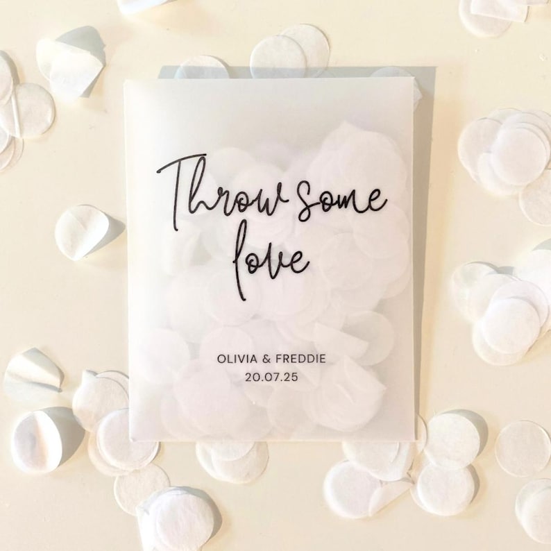Op de afbeelding: Een doorschijnende envelop gevuld met witte confetti, met de tekst "Throw some love" in sierlijke letters. Onder de tekst staan de namen "OLIVIA & FREDDIE" en de datum "20.07.25". Witte confetti is rond de envelop verspreid.