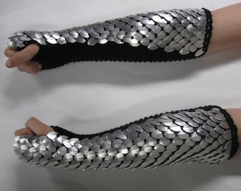 May include: A pair of black and silver arm warmers with a scale-like design. The warmers are made of a knitted fabric and have a silver metal scale design.