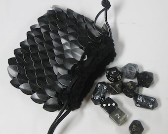 Peut inclure: Sac à dés en cotte de mailles noire avec une fermeture à cordon. Le sac est rempli de dés noirs et blancs avec des chiffres dorés.